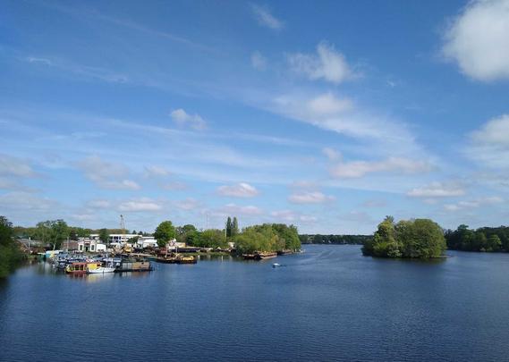 Die Havel bei Berlin: das Wasser blau, am gegenüberliegendem Ufer liegen verschiedene Boote, am blauem Himmel ein paar Schlieren.