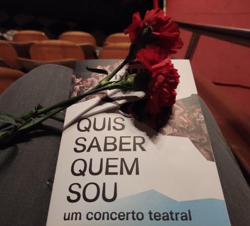 Foto do folheto do concerto teatral "Quis Saber Quem Sou" com dois cravos vermelhos pousados em cima