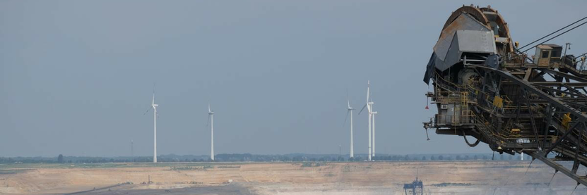 Im Vordergrund die Schaufel eines Kohlebaggers in einem Tagebau in Garzweiler. Im Hintergrund Windenergieanlagen.