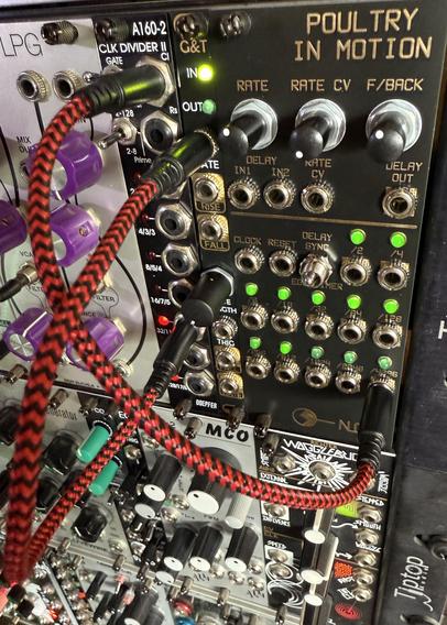 The corner of a modular synth looking down, focused on a group with black panels, mostly jacks, red and green LEDs lit up in-sync to a moment in time. Other colorful modules can be seen extending below and to the left.