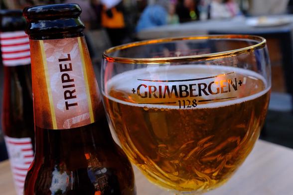 Eine leere Flasche Bier und ein volles Glas mit Bier in Nahaufnahme: Grimmbergen Triple