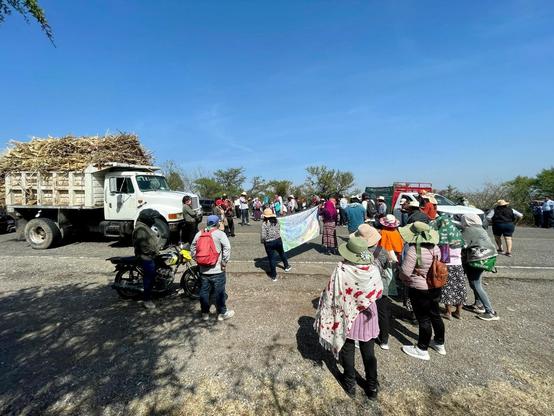 Dozens of people holding banners, along with a pickup truck, blockade a highway as a truck carrying cargo approaches.