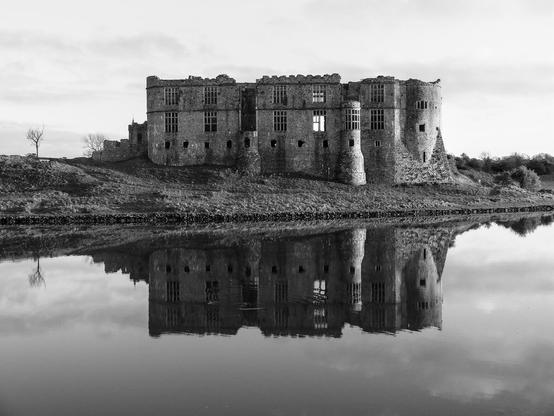 A large castle with crenellated towers and a facade full of windows is reflected in a lake.