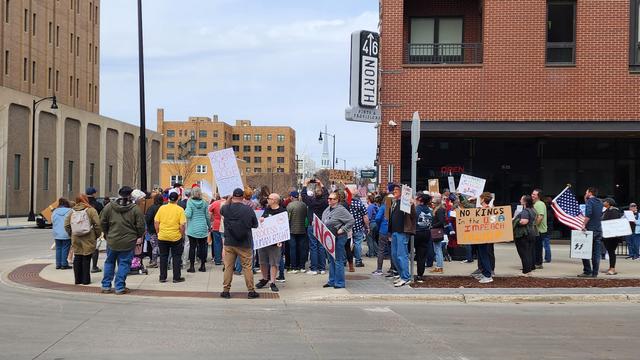 A wider shot showing 100 protestors holding signs on a city street.