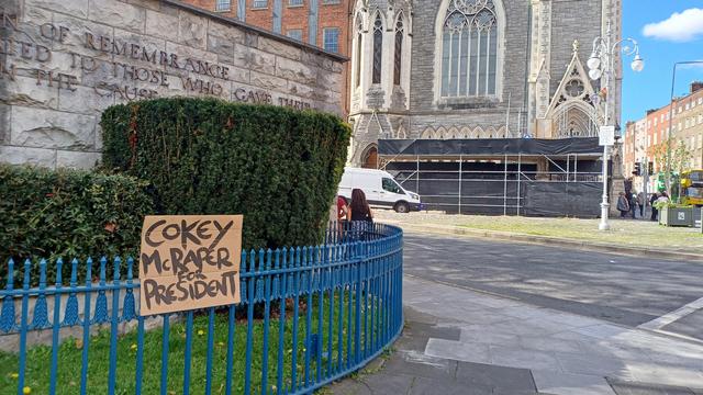 Lone handmade cardboard sign on railings, outside Garden of Remembrance,  Findlater Church in background: "Cokey McRaper for President"