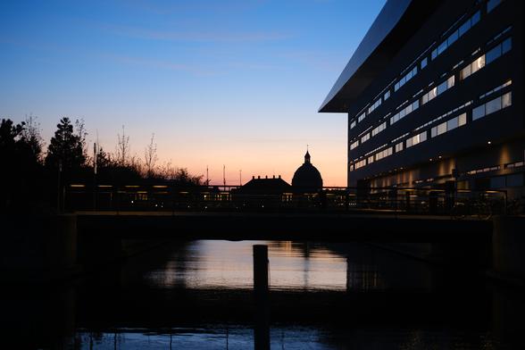 Photo of Copenhagen after sunset with water in the foreground from blue to orange and the sky from orange to blue towards the top, prominently featuring the silhouettes of Frederik’s Church and the Royal Danish Theatre.