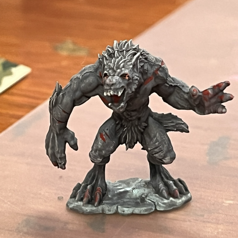 A fully painted werewolf miniature. It is gray with light highlights and darker shadows, white teeth and red on its claws and in some slashed wounds.