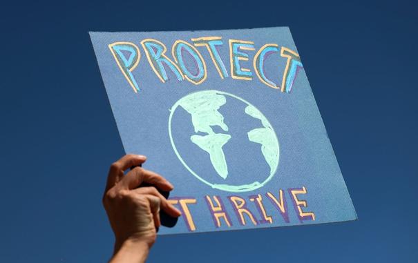 A poster is held up saying "PROTECT THRIVE"