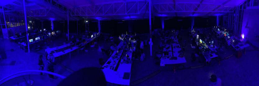 A lot of computers with displays on multiple tables. The entire room is lit by blue ambient led lights.