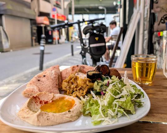A mix falafel plate with hummus, salad, chicken and pita bread. In the background a street in shinsaibashi.