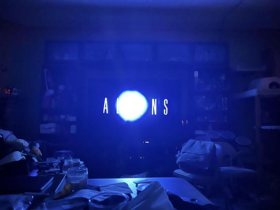 A photo of my tv, playing the title card of James Cameron’s film Aliens. The I is obscured as my phones low light camera gets confused by the fade to white. XD