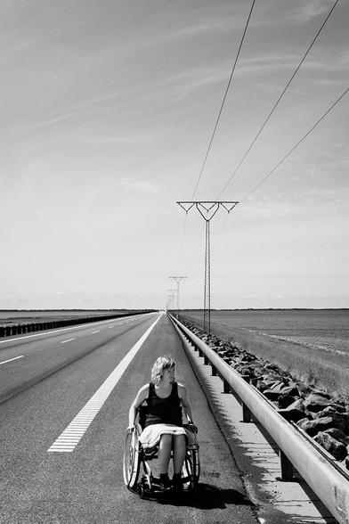 Eine Rollstuhlfahrerin ganz allein auf dem Seitenstreifen auf der einsamen Straße vom Festland nach Rømø.