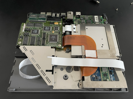 The inside of a Macintosh PoweBook 170. A white flex cable from the microSD extension spans from the BlueSCSI board to the battery slot on the opposite side.