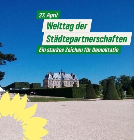 Ein Sharepic der Grünen mit einer Fotografie des Château de Sceaux und seinem Schlossgarten. Man sieht eine große Schotterfläche vor in Form geschnittenen Buxbäumen. Das Château de Sceaux ragt hinter den Hecken des Schlossgartens empor. Die ganze Szene steht unter einem wolkenlosen blauen Himmel. Unten links ist die Sonnenblume der Grünen. Oben rechts steht der Text "27. April Welttag der Städtepartnerschaften. Ein starkes Zeichen für Demokratie"