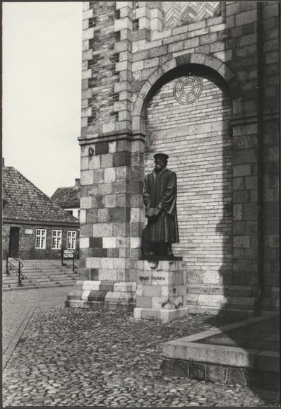 Monochrome real photographic postcard showing a view of the statue of Lutheran theologian and Bishop of Ribe Hans Tausen by Ribe Cathedral in Jutland, Denmark.

Published by HBH, not numbered.

Postally unused.

Good condition, with very slight corner bumps, but very light small bend to upper right side.