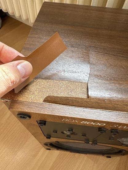 A speaker covered in plastic wood optics texture that is falling off. Underneath: particle board.