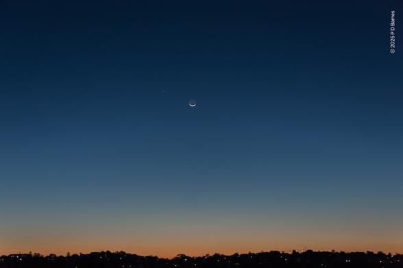 A clear blue pre-dawn sky, running the gamut of blues from almost navy through to pale eggshell and then changing to muted orange just above the horizon. Halfway up the heavens is a crescent moon, and not far away is Mercury. Along the bottom of the image runs the silhouetted dark suburban skyline, lit up sporadically with pinpoints of light.