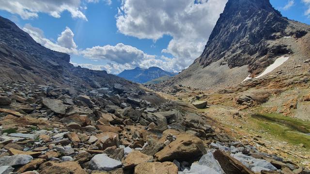 Foto einer Berglandschaft. Es zeigt den Passo della Rossa mit seinem roten Gestein. Rechts ein Gipfel.