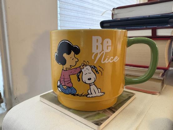 Yellow coffee mug with Lucy from the Peanuts scratching Snoopy’s head. Caption is “Be nice”