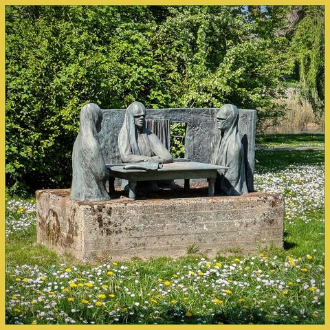 Sculptor 'De Emmausgangers' by artist Jan Haas (1941-2018) amidst a lawn with springflowers