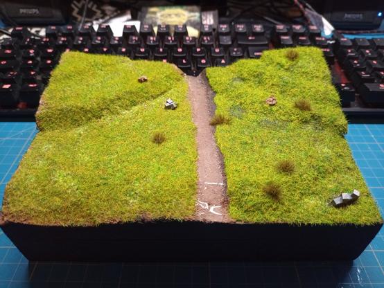Small block of scenic terrain with green hills, grass and Tufts. A small stream running down the middle.