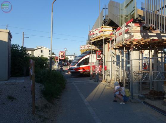 Eisenbahnkreuzung mit Triebwagen, daneben Steg in Bau