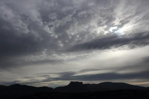 Fotografía de un paisaje de montaña a primeras hora de la mañana con el cielo nublado y un aspecto dramático. En la parte inferior de la imagen, las siluetas oscuras de las montañas. El resto de la foto está compuesta por el cielo y las nubes.