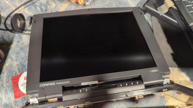 The top housing and screen of a Compaq Presario 1220 laptop. It's been removed from the lower housing and is resting on a table. The screen is in surprisingly good shape given the age of the computer!