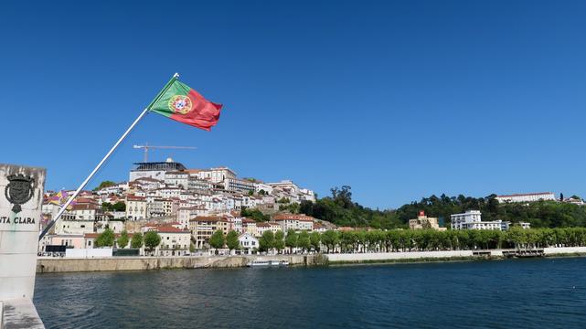 Landscape of the city of coimbra and Mondego river. In front, a portuguese flag on a bridge.