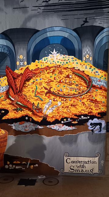 Une partie de la tapisserie de Smaug, où on voit Smaug sur son tas d'or, narines fumantes, face à une petite silhouette noire qui représente Bilbo dissimulé grâce à l'Anneau