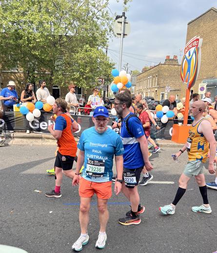 Runners on a road. A middle-aged white man is facing the camera. Spectators in the background. Festive atmosphere.