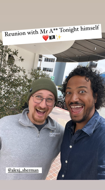 Instagram story with a selfie of Alex Sherman and Samba Schutte standing outside a building. They are both grinning with their mouths wide open. Text above the photo reads, “Reunion with Mr Ass Tonight himself (3 emojis: red heart, pirate flag, sparkles).” AlexJ_Sherman has been tagged at the bottom.