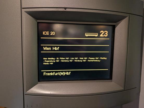an old looking but quite high contrast monochrome LCD of a relatively small pixel density, the individual pixels are not hard to spot. it's surrounded by gray plastic in a circular shape, as if it were part of a wall (i don't know how to describe it any better). in white text on a black background it says "ICE 20", "Wien Hbf", "Frankfurt(M)Hbf" and other stations in between. the design is very simple, the font looks like a normal sans-serif typeface though with some geometric or "mechanical" elements - it may have been upscaled from a smaller size