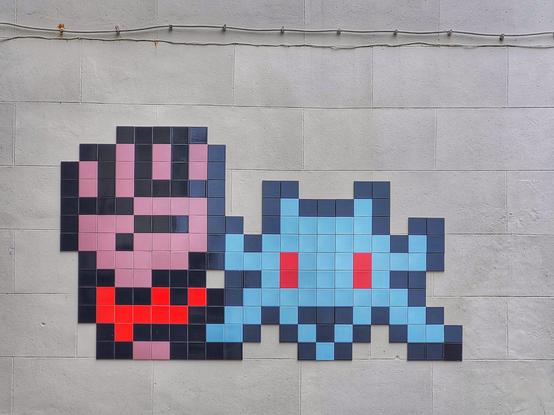 Un space invader bleu aux yeux rouge, accompagné d'un poing levé avec un bracelet rouge