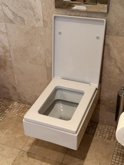 Eine wandmontierte rechteckige Hotel-Toilette von beigen Marmorplatten umgeben.
