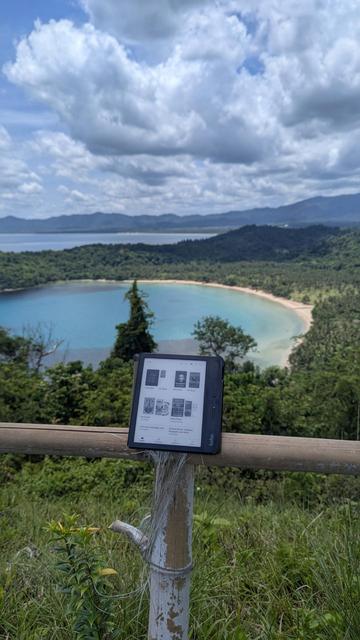 Overlooking view with Kobo ereader at the center of the photo. Blue sky and clouds about with mountains and the sea below.