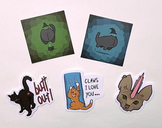 stickers! of my cat art. various art includes 'butt out!' — a perturbed black cat looking back & exposing it's butt; a punk-rock sphinx cat with ear & nose piercings and pink meowhawk; an orange tabby shreds curtains with text 'claws i love you…'; 2 different levitating cat stickers 'wearing' a pointed black witch-hat suspended above its head, one with a green background floats above a smouldering cauldron. the second stealthy cat floats on a blue background