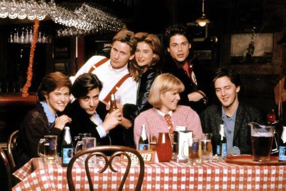 Cast of St Elmo's Fire around a table with a checkered tablecloth, an assortment of drinks on it