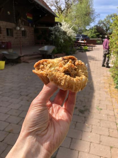 Nahaufnahme eines leckeren Karotte-Nuss-Muffins mit Käsekuchenfüllung in meiner Hand. Im Hintergrund ein Hofgebäude.