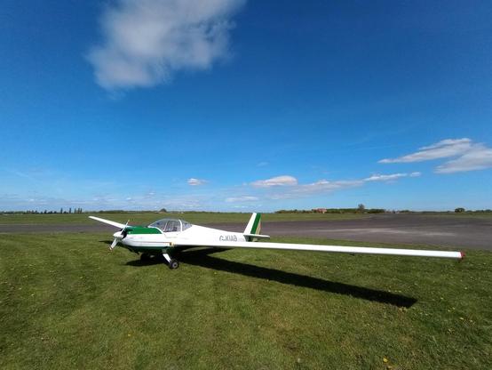 A motorglider sits on a grassy patch on a bright sunny day