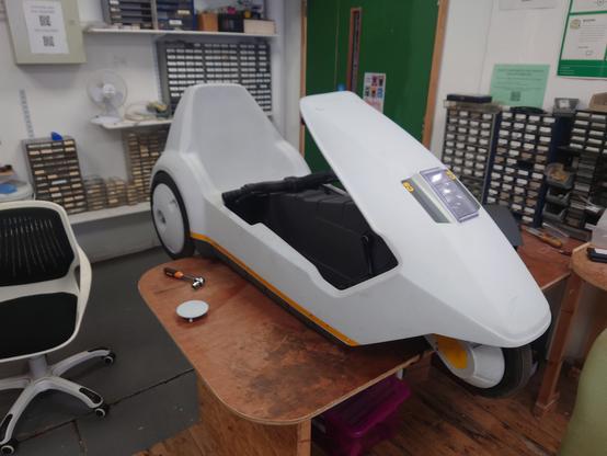 The Sinclair C5 on a table in Nottingham Hackspace's electronics lab, with the wheels hanging off each end of the table.