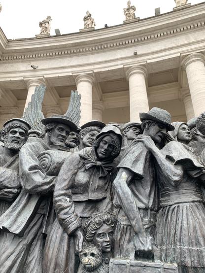 Ausschnitt der Skulptur „angels unawares“ auf dem Petersplatz in Rom. Einer der dargestellten Migranten trägt einen Hund, dessen Nase von vielen Betatschen bereits die Patina verloren hat und goldig glänzt.