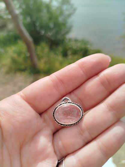 a silver pendant with transparent oval stone. it has a dangled copper wire underneath the stone. it's hold on a hand