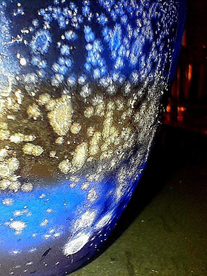 Ice condenses on the exterior of a blue glass tumbler with ice frozen into the bottom, with subzero Jägermeißter, resembles an ice moon.