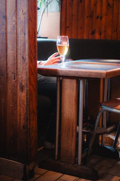 A table in a brown bar. There’s a beer on the table and the sun is shining through.