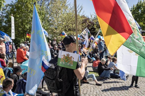 Eine Person ist mit Freie-Sachsen- Deutschland- und Friedensfahnen behängt.