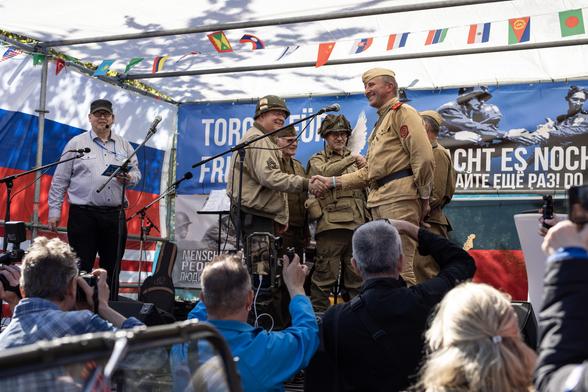 Reenactment-Darsteller stellen das historische Handschlag-Foto von Torgau auf der Bühne nach. Vor der Bühne stehen zahlreiche Menschen, die das mit ihren Kameras festhalten.
