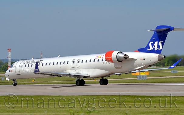 Side view of a long, thin, white, twin engined jet airliner with the engines mounted on the sides of the rear fuselage.
The plane is moving from right to left and slightly away from the camera on a grey runway.
The plane is almost entirely white, with silver "Scandinavian" titles on the upper forward fuselage, just above the first few passenger cabin windows, with even whiter "Airlines" titles on the lower forward fuselage, under the windows.
The registration "EI-FPJ" is on the lower rear fuselage, under the last of the windows, just in front of the red engine pods.
The tail is a deep blue, with white "SAS" titles.
The engine pods are red at the front, with small white "Scandinavian" titles.
The upturned wingtips are the same blue as the tail, with the same "SAS" logo.
Green grass fills the foreground, with the odd stray branch of small trees at the bottom.
More grass leads off to trees lining the airfield perimeter in the distance, under grey-blue skies.