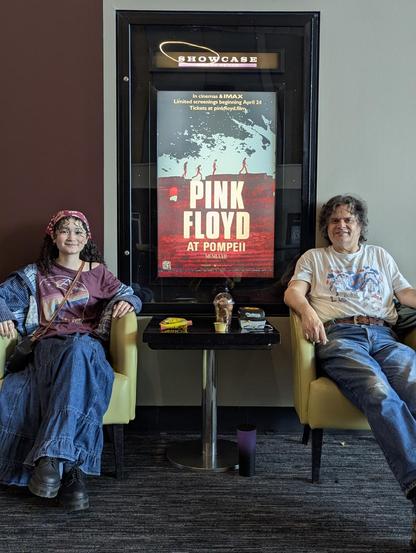 My daughter and I sitting in chairs in a movie theater lobby in front of the poster for Pink Floyd Live at Pompeii.