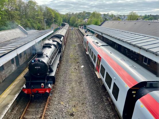 Looking down on two trains at a station the one on the left a steam train the one on the right a diesel multiple unit